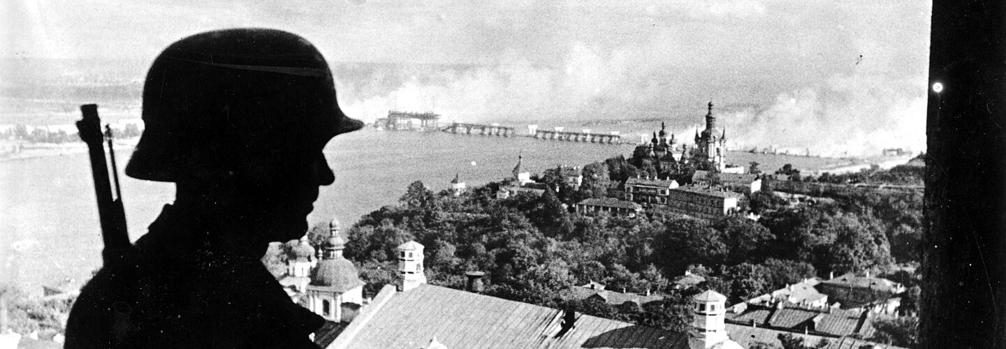 Deutscher Wachtposten in Kiew, 19. September 1941 Ein deutscher Soldat steht auf der Zitadelle in Kiew. Im Hintergrund sind das Höhlenkloster („Kloster Laora“) und die brennende Brücke über den Fluss Dnjepr zu sehen.