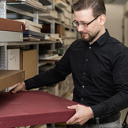 Arbeit im Archiv Ein Archivar des Bundesarchivs nimmt Archivalien aus einem Regal eines Magazins., Quelle:
<span class="nanospell-typo">BArch</span>, B 198 Bild-2017-0301-031 / Nobel, Jürgen