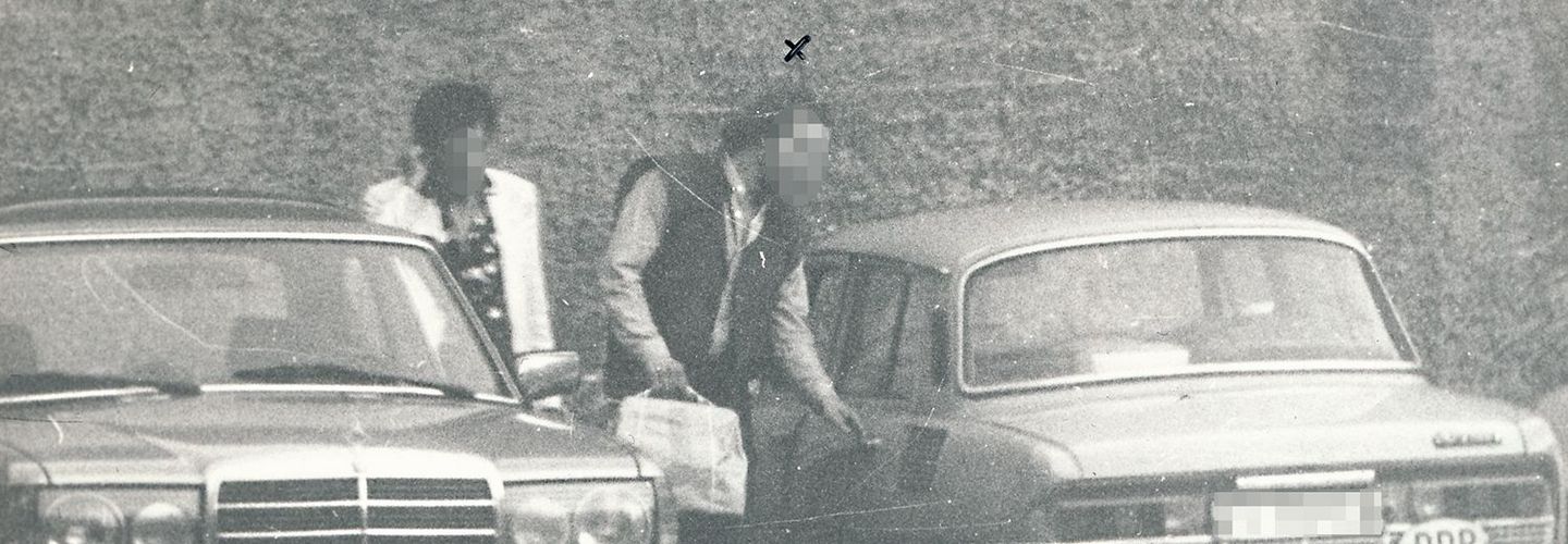 MfS-Beobachtungsfoto im Rahmen des OV "Kassette": Übergabe geschmuggelter Waren auf einem Parkplatz, 1987 Zwei Männer zwischen zwei Autos stehend