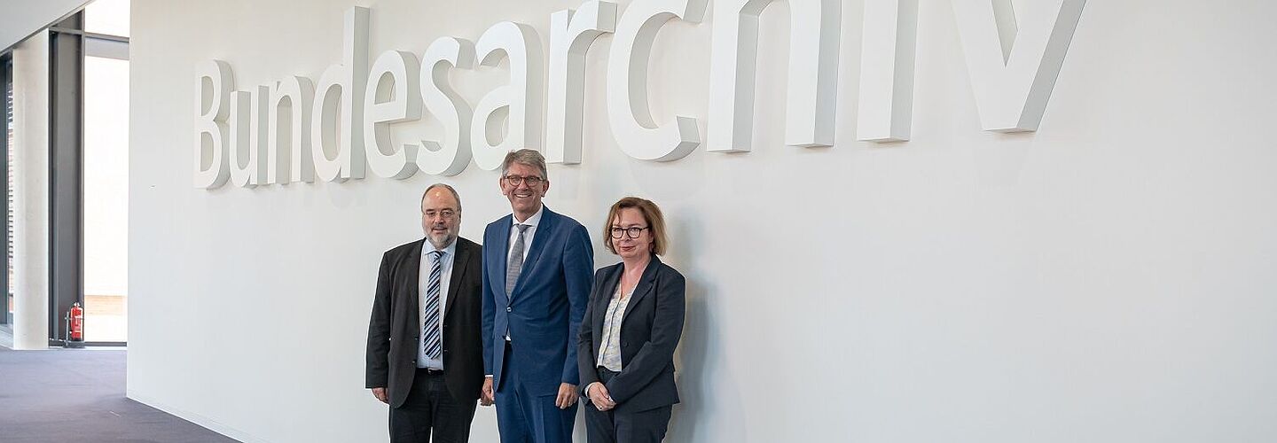 Michael Hollmann, Wolfram Weimer und Andrea Hänger im Foyer des Bundesarchiv-Standorts Berlin-Lichterfelde Michael Hollmann, Wolfram Weimer und Andrea Hänger stehen im Foyer des Bundesarchiv-Standorts Berlin-Lichterfelde vor dem Schriftzug „Bundesarchiv“.
