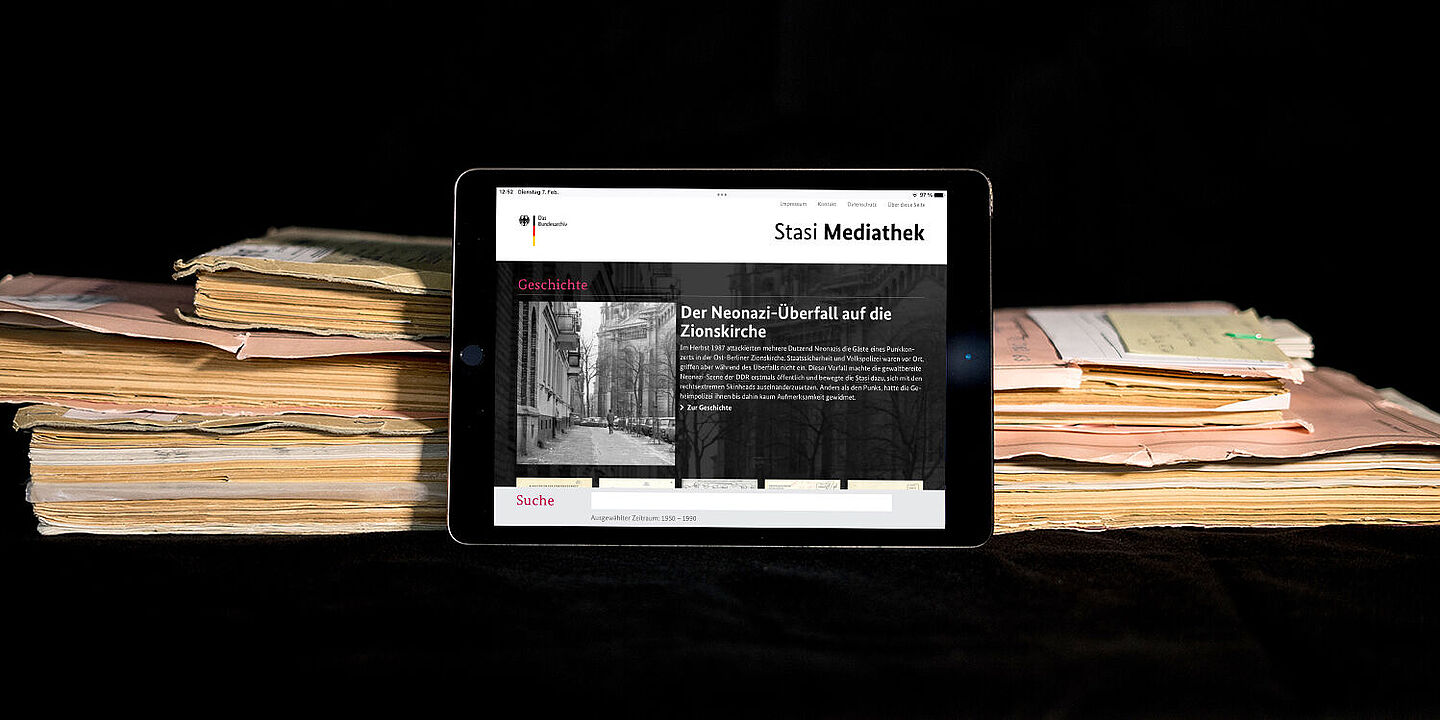 Stasi-Mediathek Das Bild zeigt die auf einem Tablet geöffnete Startseite der Stasi-Mediathek. Das Tablet lehnt an einigen Aken., Quelle:
BStU / Mulders