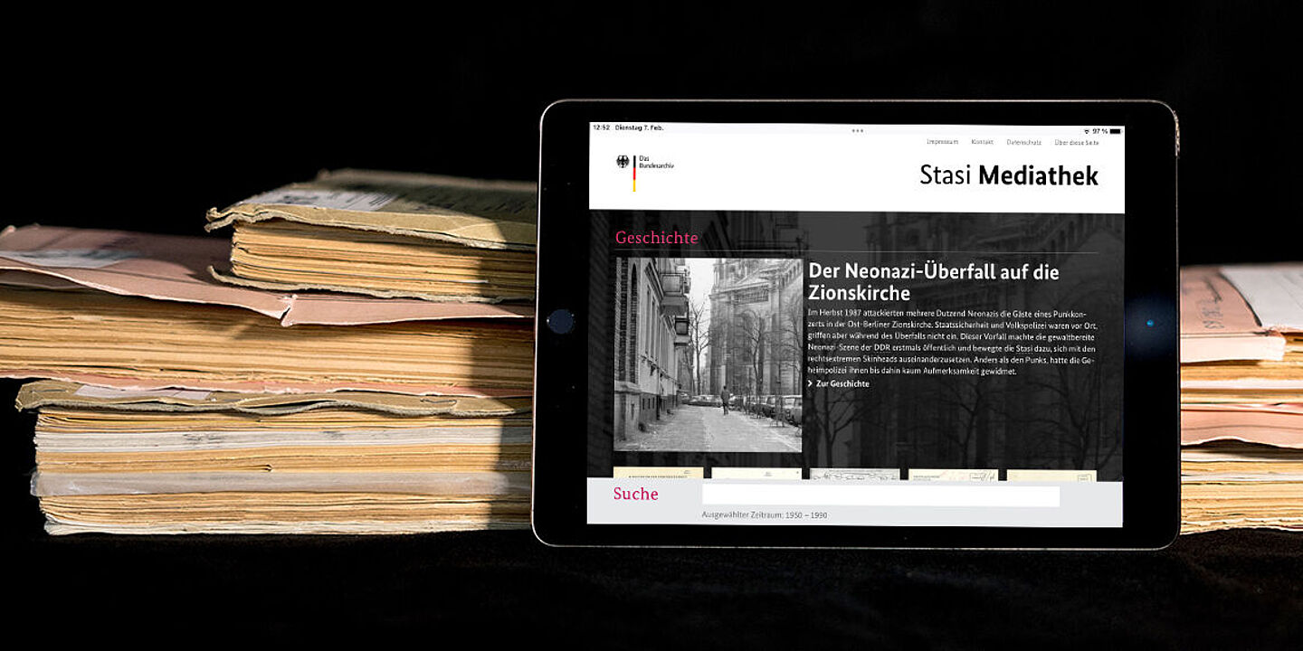 Stasi-Mediathek Das Bild zeigt die auf einem Tablet geöffnete Startseite der Stasi-Mediathek. Das Tablet lehnt an einigen Aken., Quelle:
BStU / Mulders
