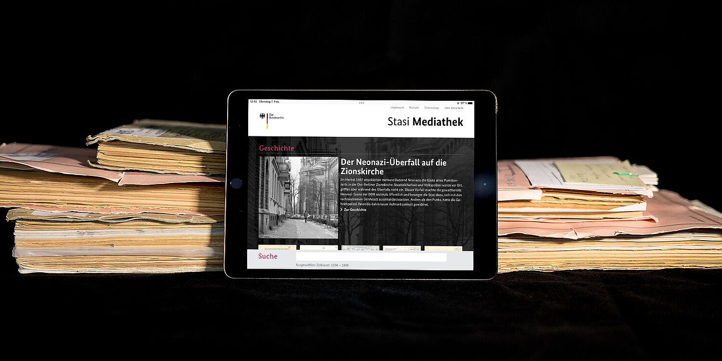 Stasi-Mediathek Das Bild zeigt die auf einem Tablet geöffnete Startseite der Stasi-Mediathek. Das Tablet lehnt an einigen Aken., Quelle:
BStU / Mulders